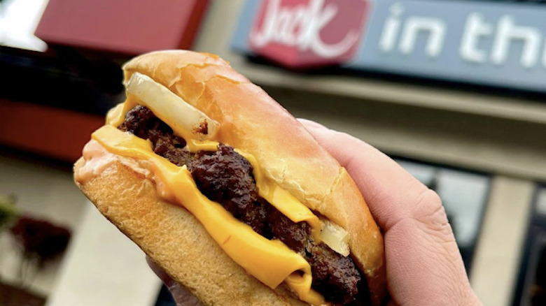 Hand holding burger in front of Jack in the Box