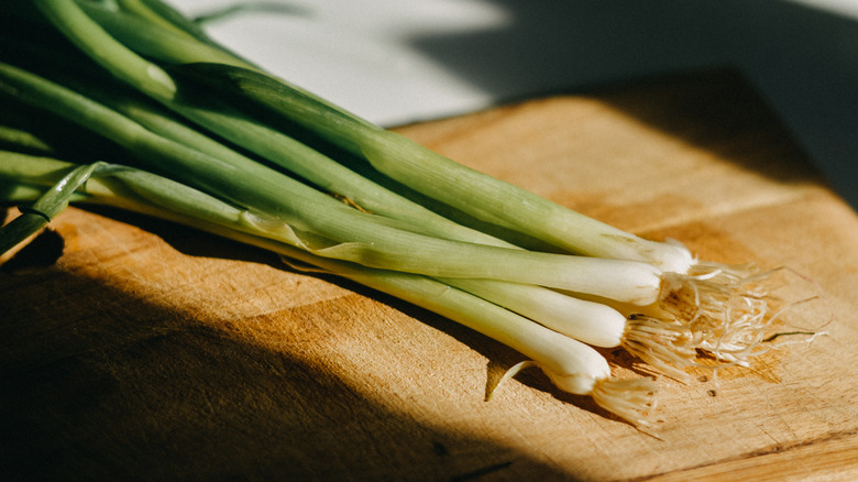 A bunch of green onions on a wooden cutting board