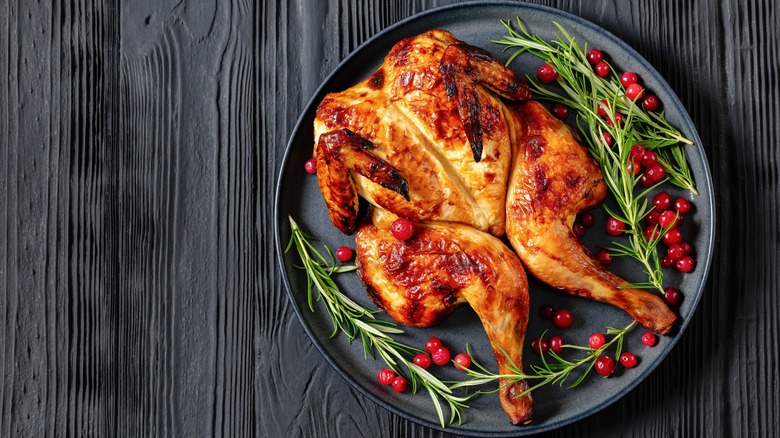 Spatchcocked roasted chicken on plate with rosemary and red currants