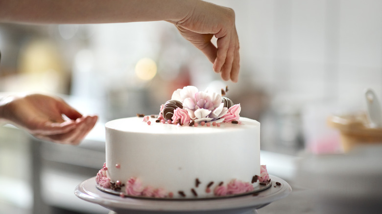 closeup of hands decorating cake with icing and flowers