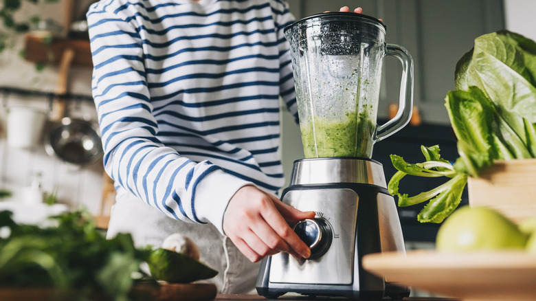 Young woman mixing green ingredients in a blender