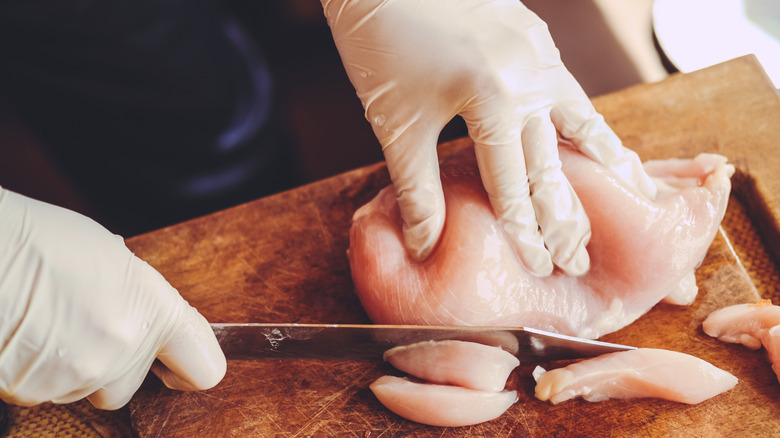 hands slicing raw chicken