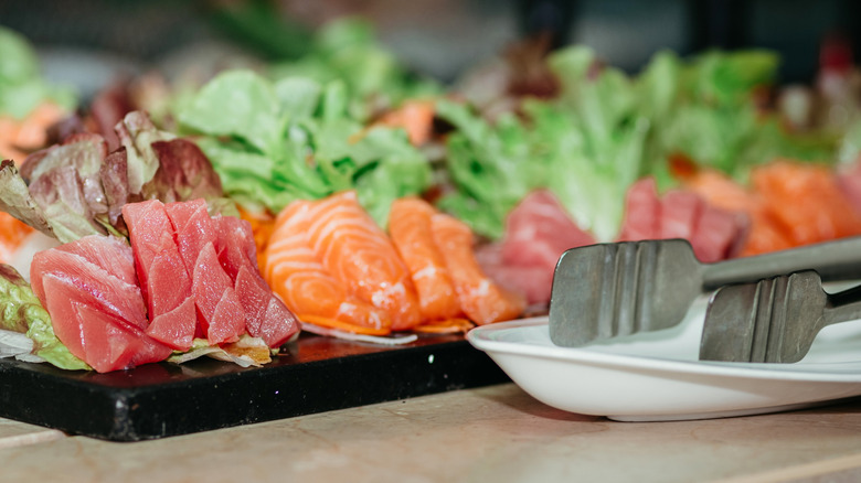 Sashimi plate and lettuce leaves on black plate by tongs