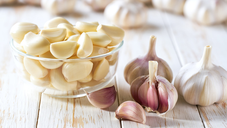 Bowl of peeled garlic cloves alongside heads of fresh garlic