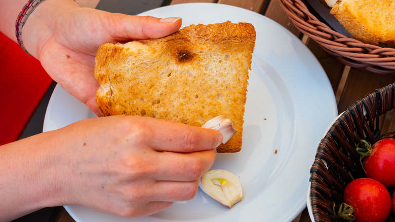 Hands rubbing garlic on toast