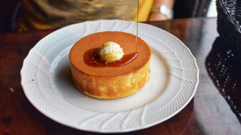 A big, fluffy pancake served on plate with maple syrup and cream.