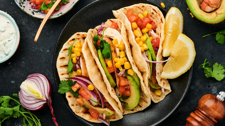 Chicken tacos on flour tortillas with avocado, tomatoes, and corn