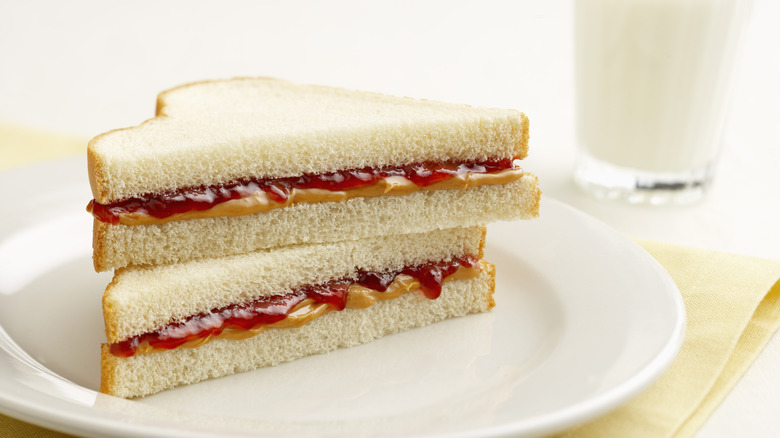 A PB&J sandwich on white bread next to a glass of milk