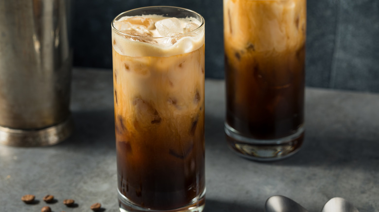 Two shaken iced espresso drinks in high ball glasses on a grey countertop