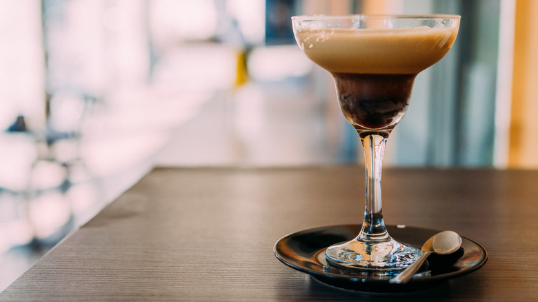 A shakerato in a cocktail coupe on a wooden table with a spoon on the side