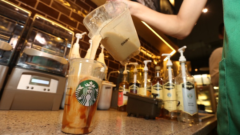 A Starbucks barista adding dairy from a blender to a Starbucks drink.