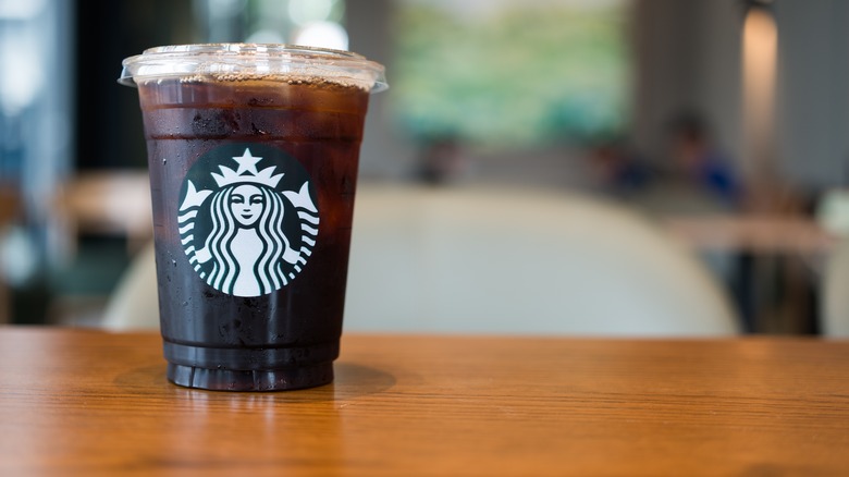 A black coffee in a plastic Starbucks cup on a wooden surface