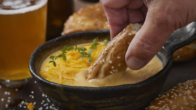 a bowl of beer cheese getting dipped with a pretzel