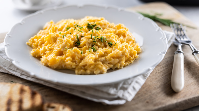 A plate with soft scrambled eggs on it beside two forks on a wooden surface