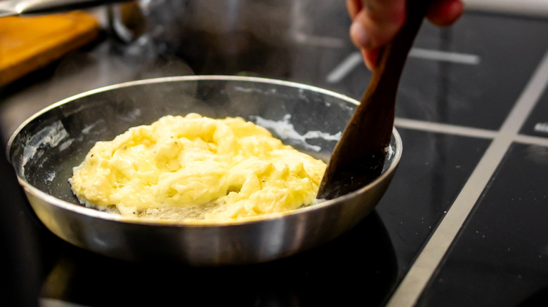 A person stirring a pan with scrambled eggs within it