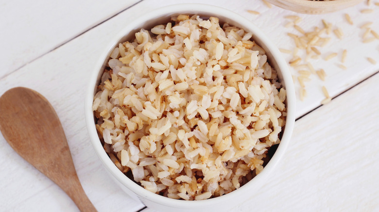 A bowl of fluffy brown rice with a wooden spoon on a white background