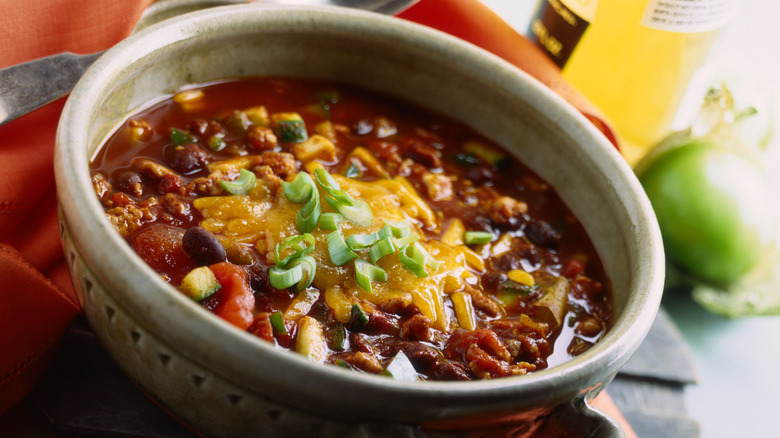 A bowl of chili with beans topped with cheese and scallions