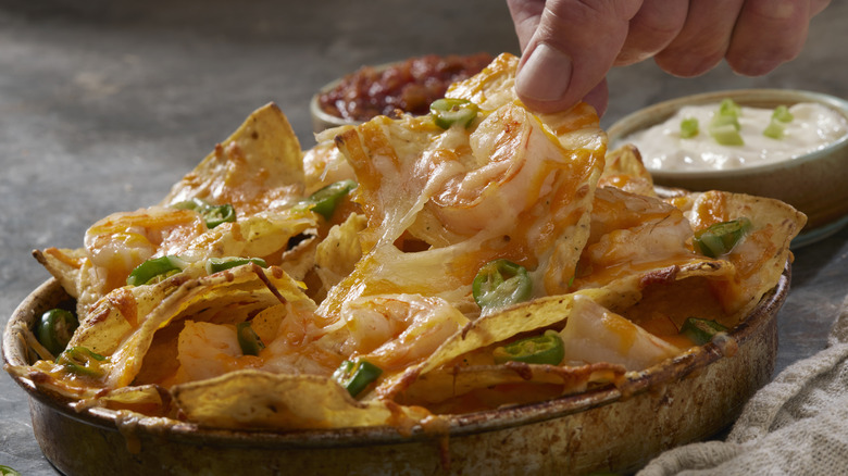 Fingers picking up nachos with shrimp