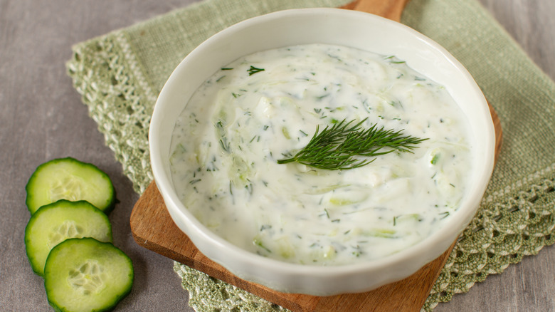 A bowl of tzatziki with fresh dill and sliced cucumbers