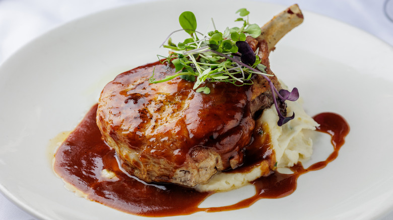 Cooked bone-in pork chop on a white plate with mashed potatoes and sauce