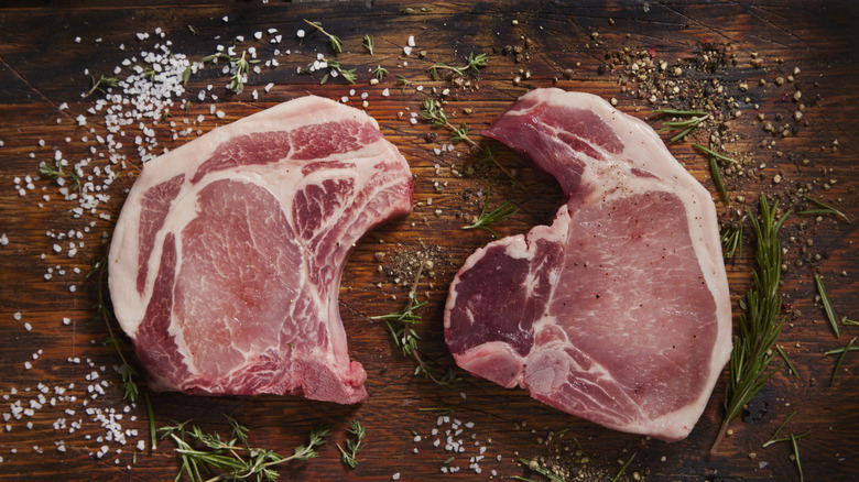 Raw bone-in pork chops on a wooden board with seasonings