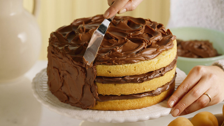 person spreading chocolate frosting on cake