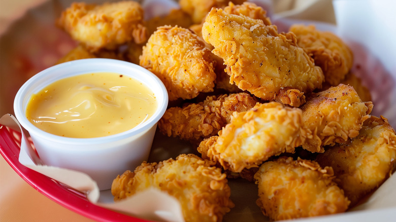 Fried chicken nuggets in red basket with yellow dipping sauce