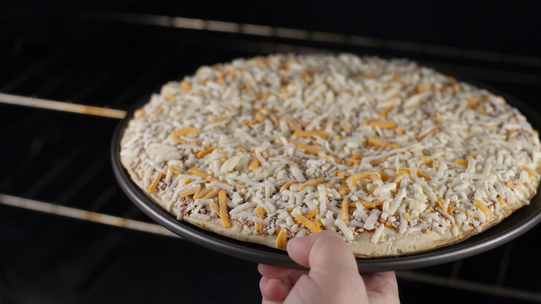 Person puts frozen cheese pizza into oven