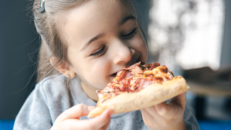 Child eating slice of meat pizza