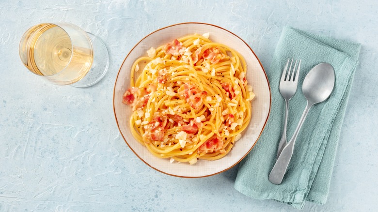 Dish of spaghetti alla carbonara next to glass of white wine and cutlery