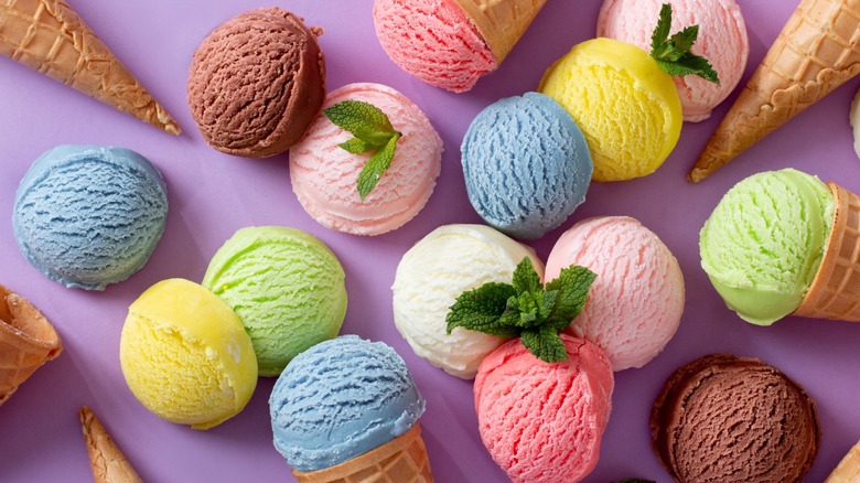 Assorted scoops of flavored ice creams scattered on a purple background with sugar cones.