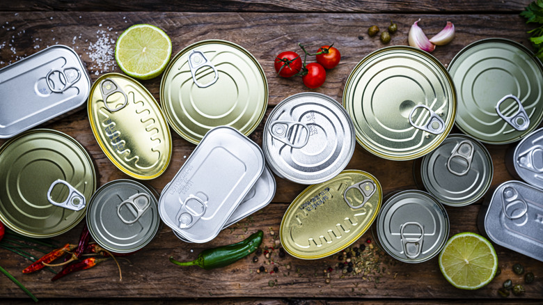 many different cans of food arrayed on a wooden table with limes, chiles, and tomatoes