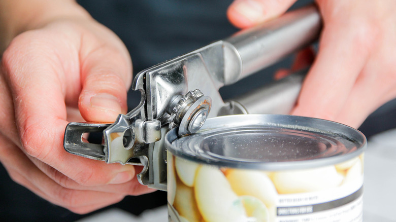 hands opening a can of beans with a can opener