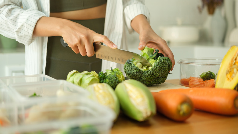 a woman chopping a crown of broccoli with other vegetables in foreground