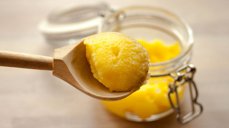 A wooden spoon with a scoop of ghee on it in front of a jar of ghee