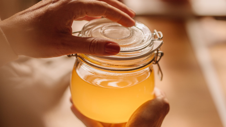 A person holding a glass jar full of clarified butter