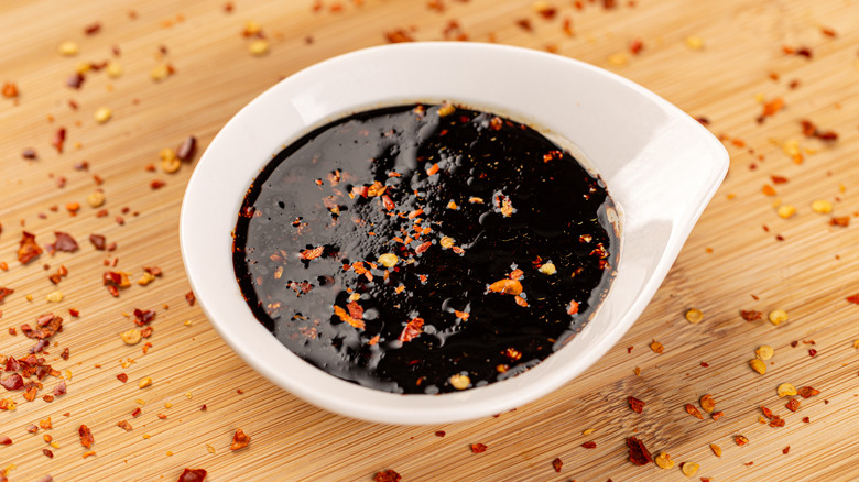 Teriyaki sauce with pepper flakes on top in a small bowl on a bamboo board