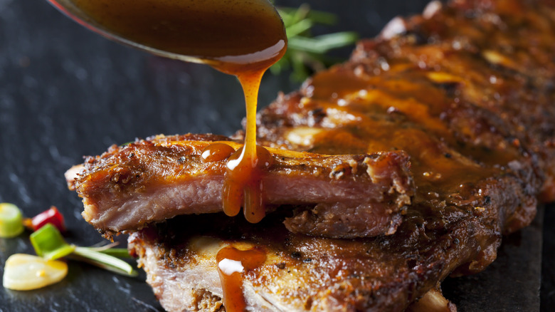 Up close picture of ribs coated in bbq sauce with a spoon drizzling more sauce onto the ribs