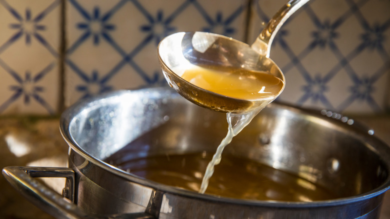 A ladle drips broth into a large pot containing more broth