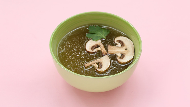 A small green bowl mushroom broth against a pink background