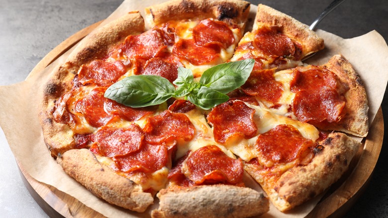 pepperoni pizza garnished with basil leaves sitting on a wooden plate covered with brown paper