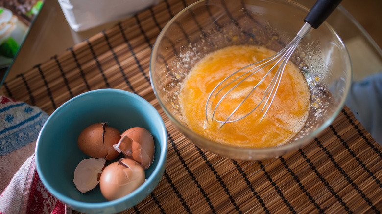 A mixing bowl filled with a whisked egg beside a bowl of egg shells