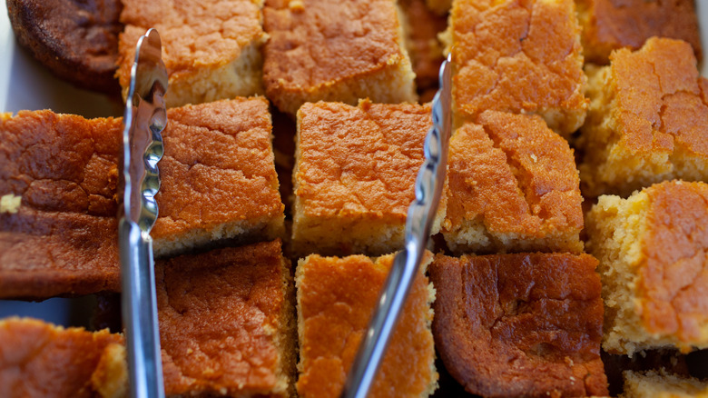 Squares of cornbread covered by metal tongs.