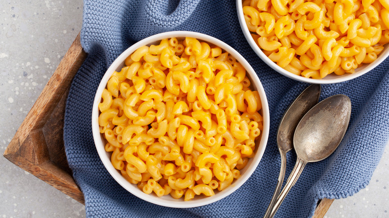 Two bowls of mac and cheese sitting on a trays with two spoons beside them