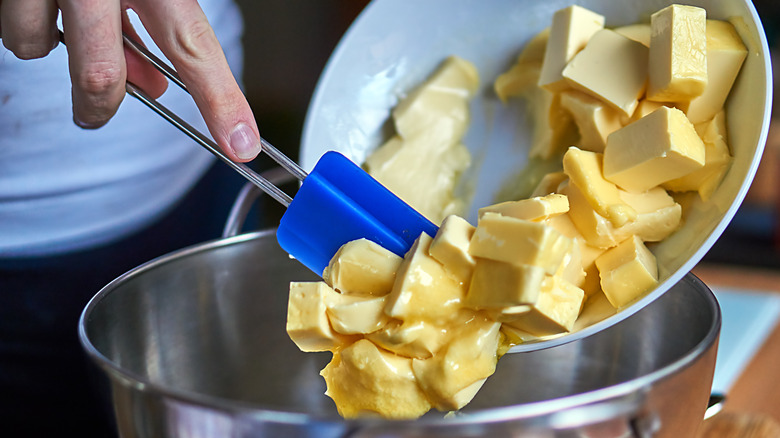 Butter cubes being placed in a mixing bowl with a blue spatula.