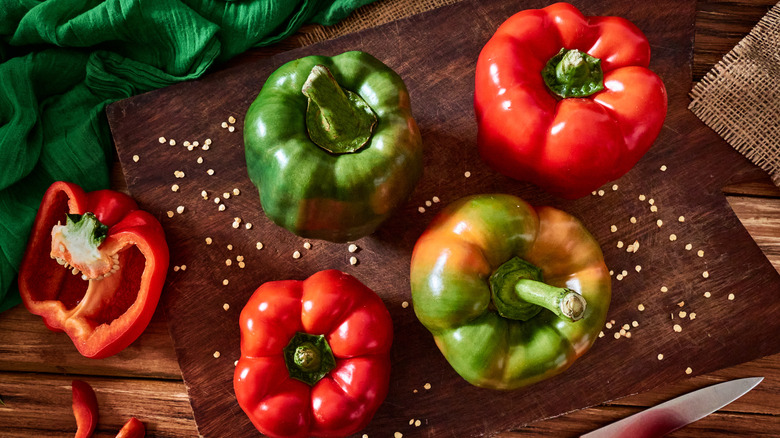 Green and red bell peppers sitting on a cutting board with seeds scattered