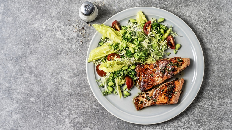 Plate of seared salmon and salad with tomatoes, lettuce, broccoli, and edamame