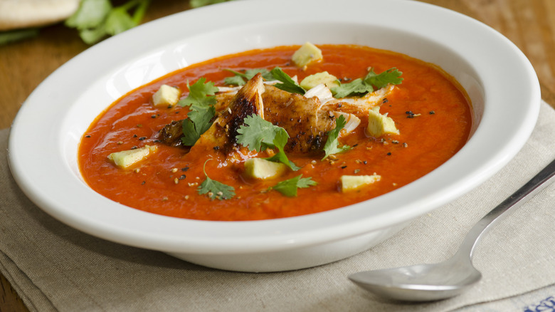 Bowl of tomato soup with chicken, avocado, and herbs