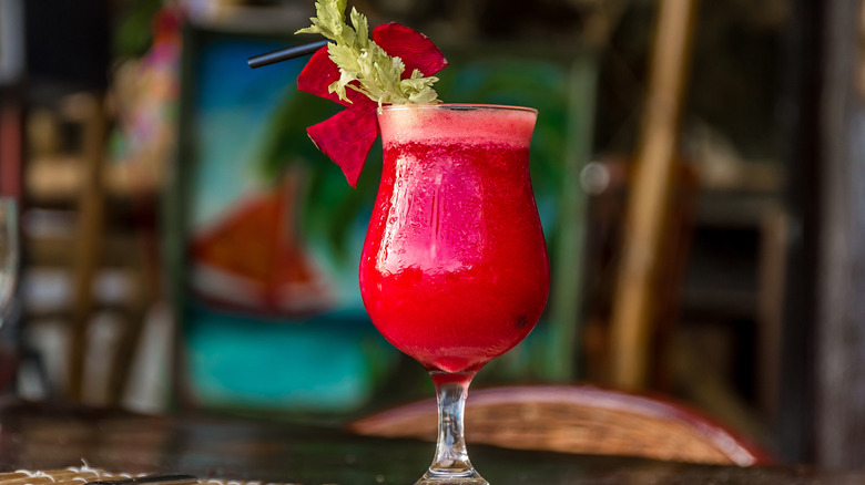 An alcoholic beetroot juice cocktail with celery garnish in a hurricane glass