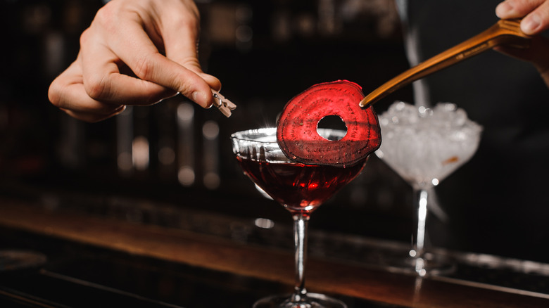 A bartender carefully putting a slice of beet onto a cocktail glass rim